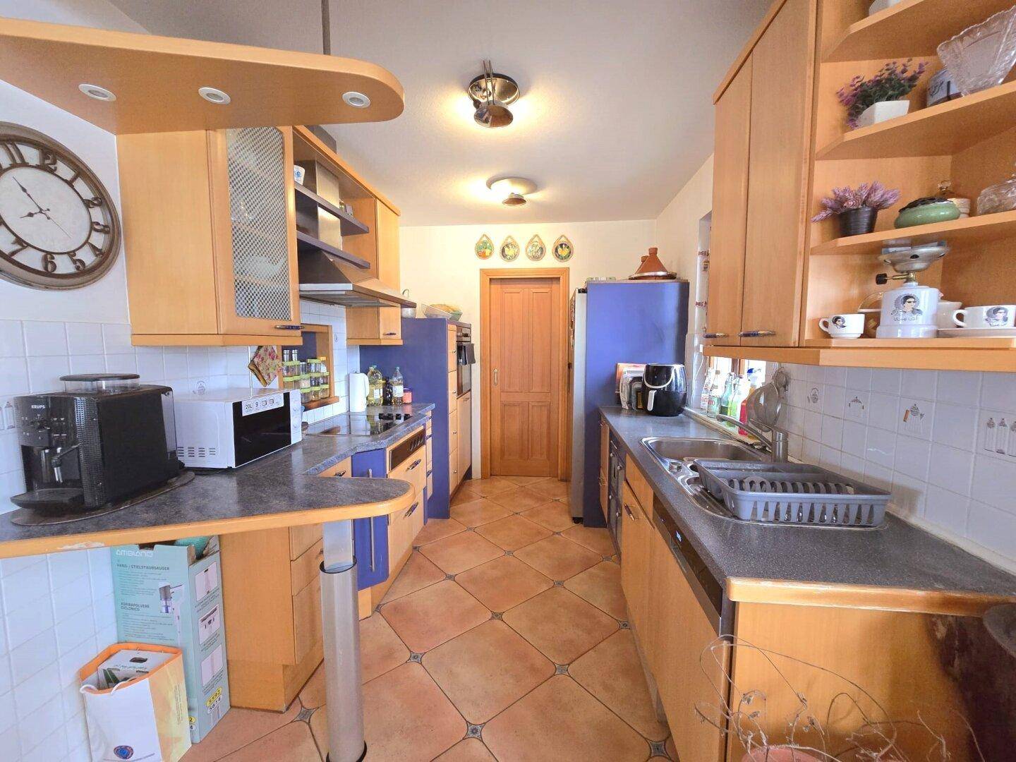 Funktionale Küche mit Holzschränken, Fliesenboden und integrierten Geräten.