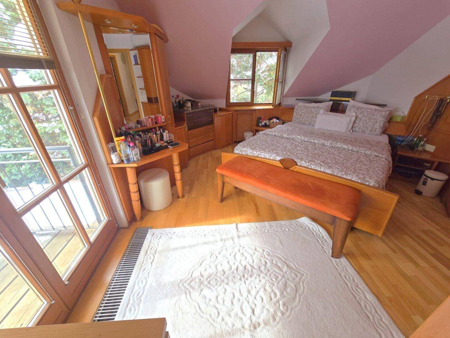 Schlafzimmer im Dachgeschoss mit Holzboden, Schminktisch und Zugang zum Balkon.