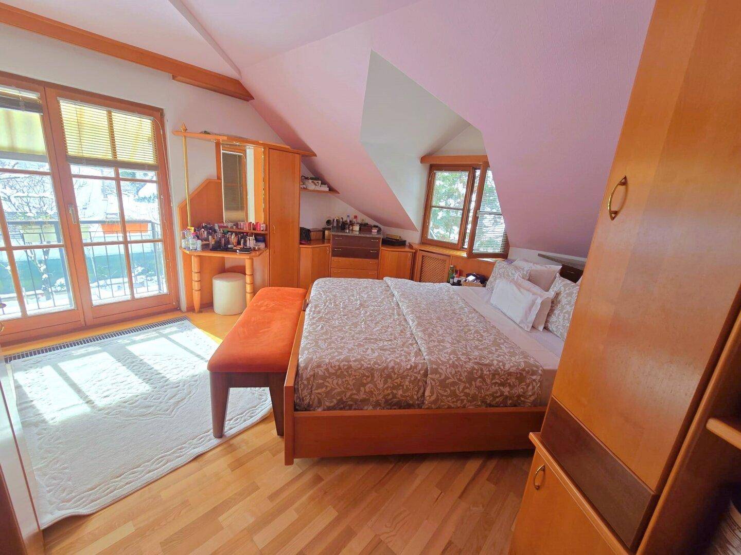 Helles Schlafzimmer im Dachgeschoss mit Holzboden, Schminktisch und Balkonzugang.