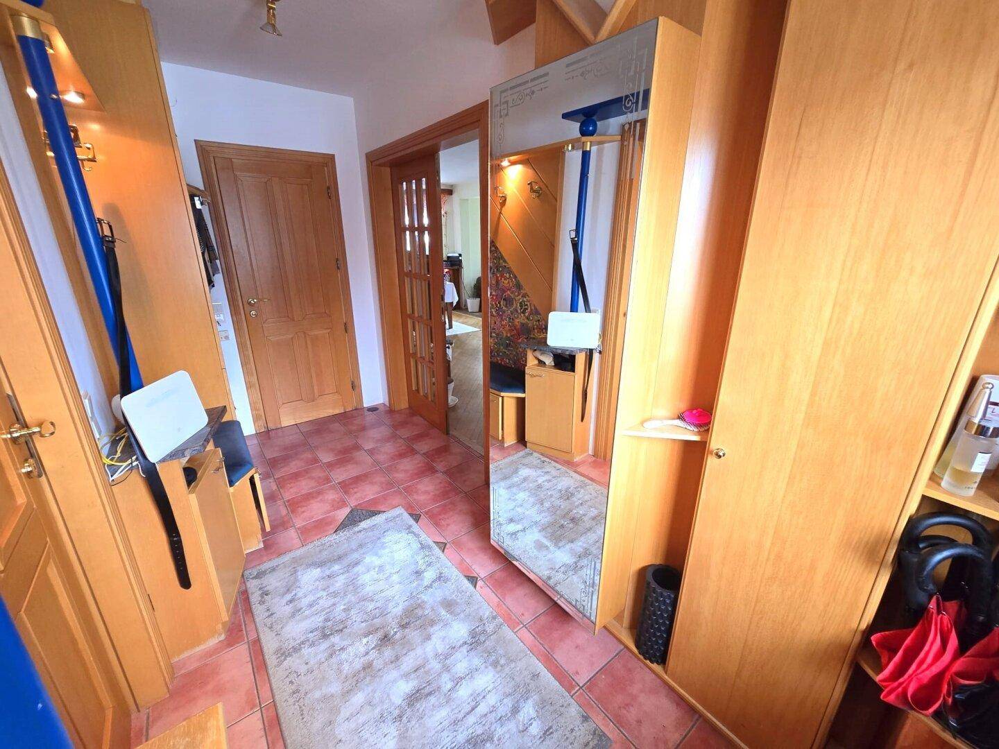 Eingangsbereich mit Fliesenboden, Holzschränken und einem großen Spiegel.