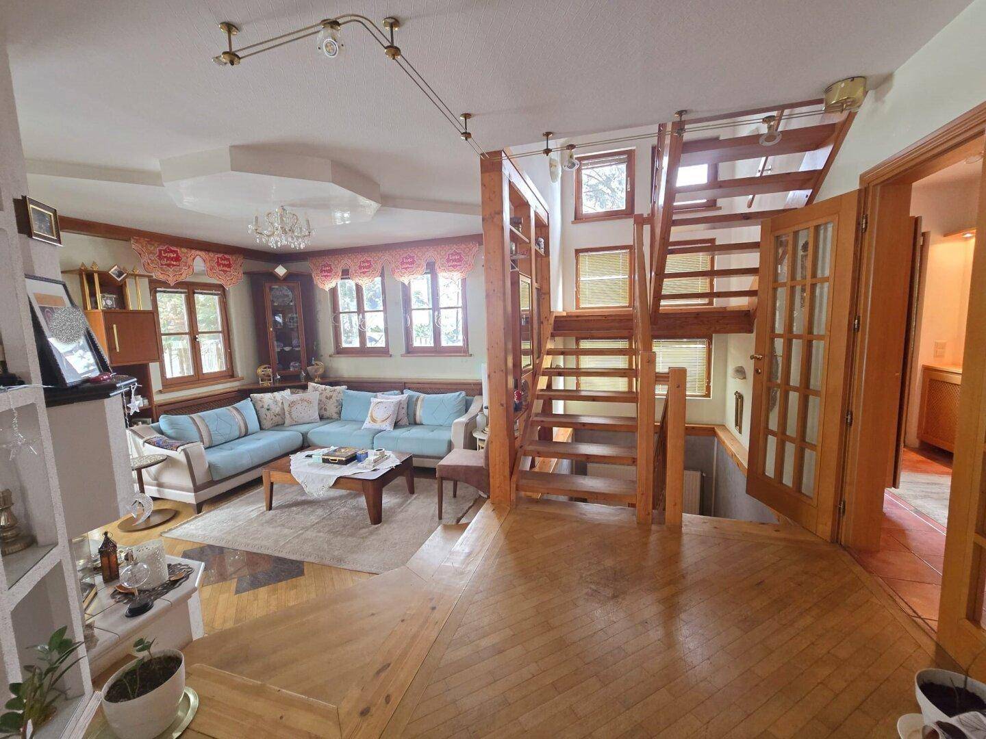 Gemütliches Wohnzimmer mit großem Sofa, Holzboden und offener Holztreppe.