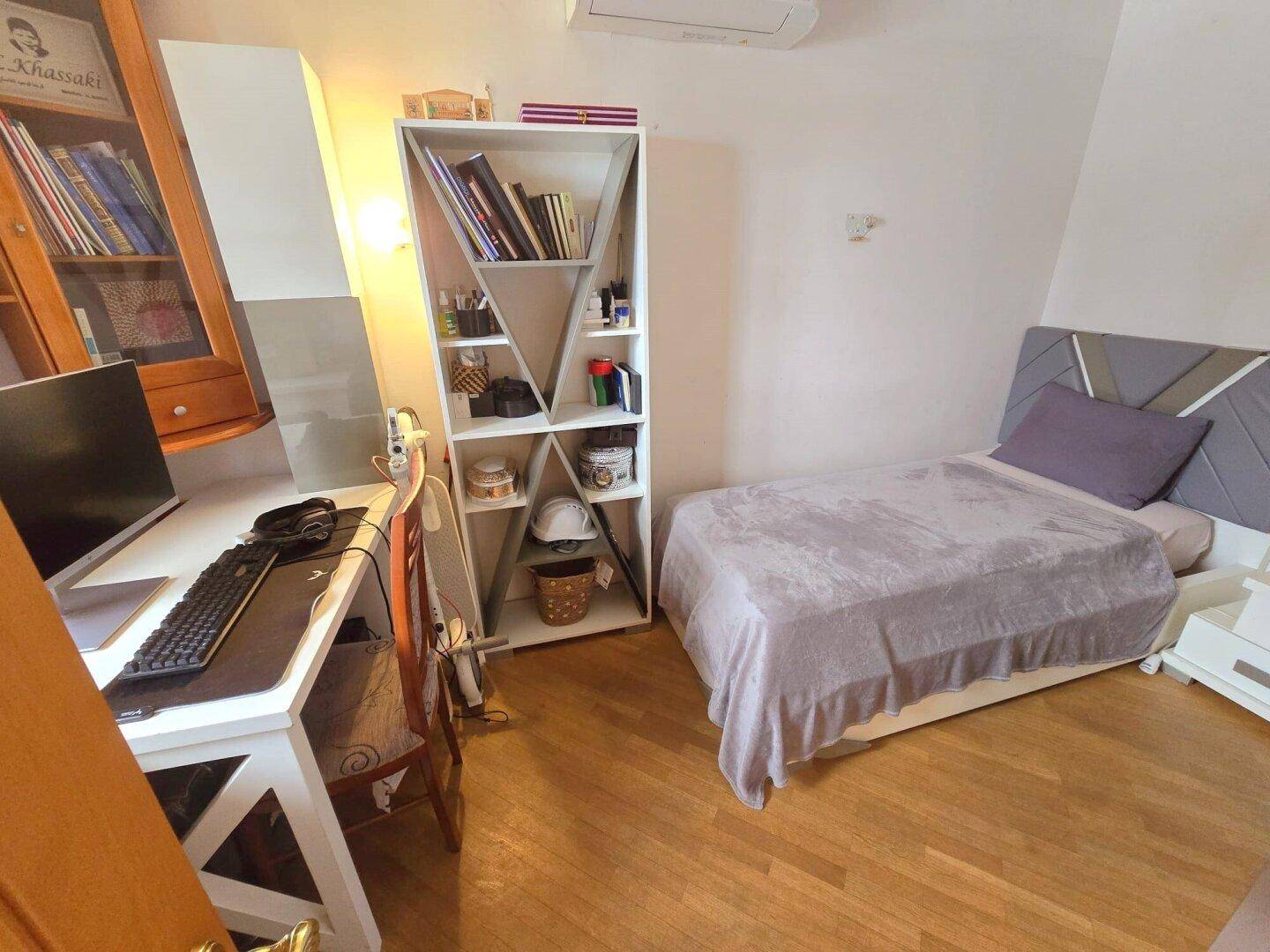 Schlafzimmer mit Holzboden, Schreibtisch und Klimaanlage.