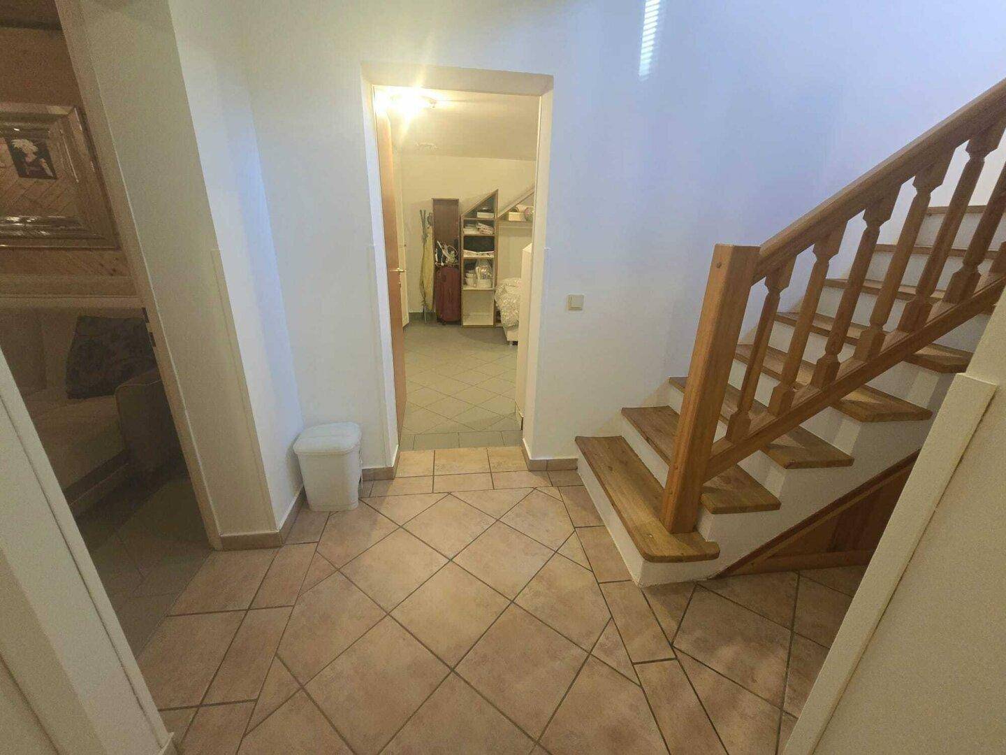 Heller Flur mit gefliestem Boden und Holztreppe, die in den oberen Bereich führt.