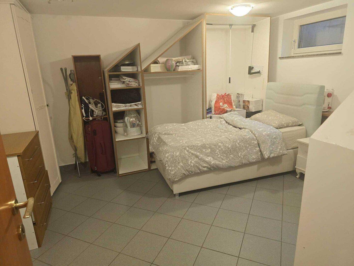 Schlafzimmer im Untergeschoss mit Fliesenboden, Bett und Stauraum unter der Dachschräge.