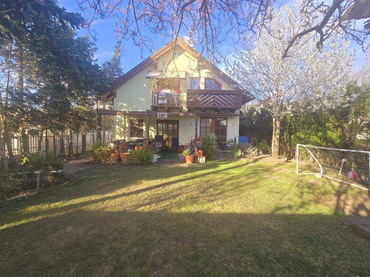Sonniger Gartenbereich mit Rasen, blühenden Bäumen und einer Terrasse am Haus.