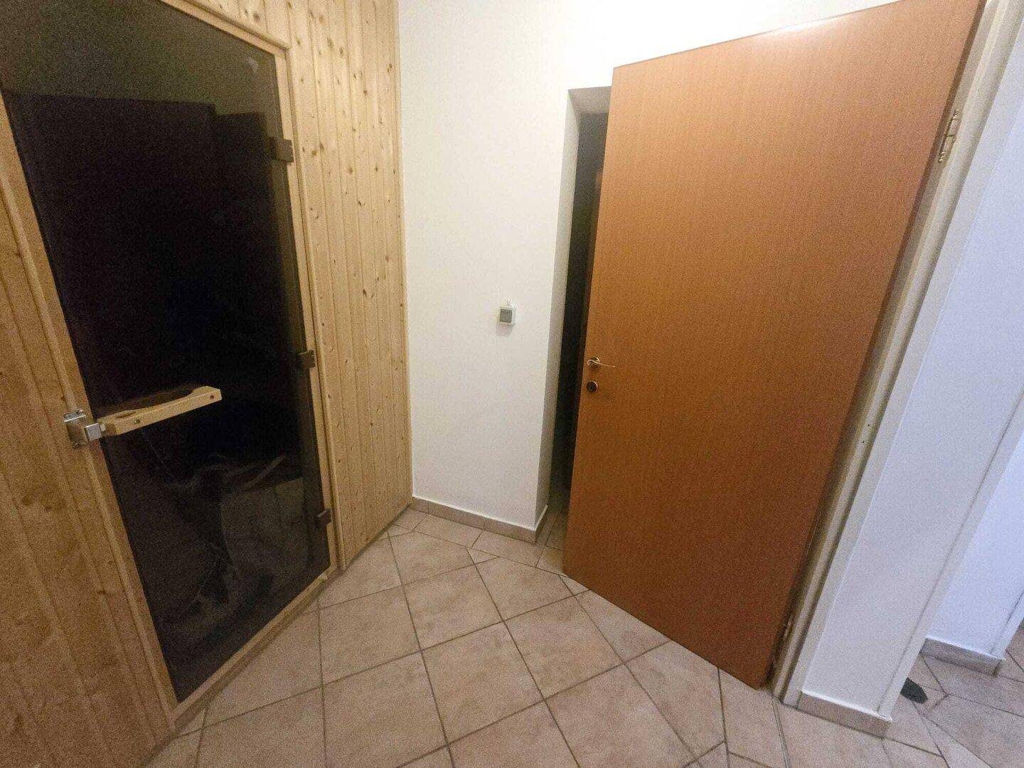 Kleiner Raum mit einer Holzkabine, die eine Sauna beherbergt, und gefliestem Boden.