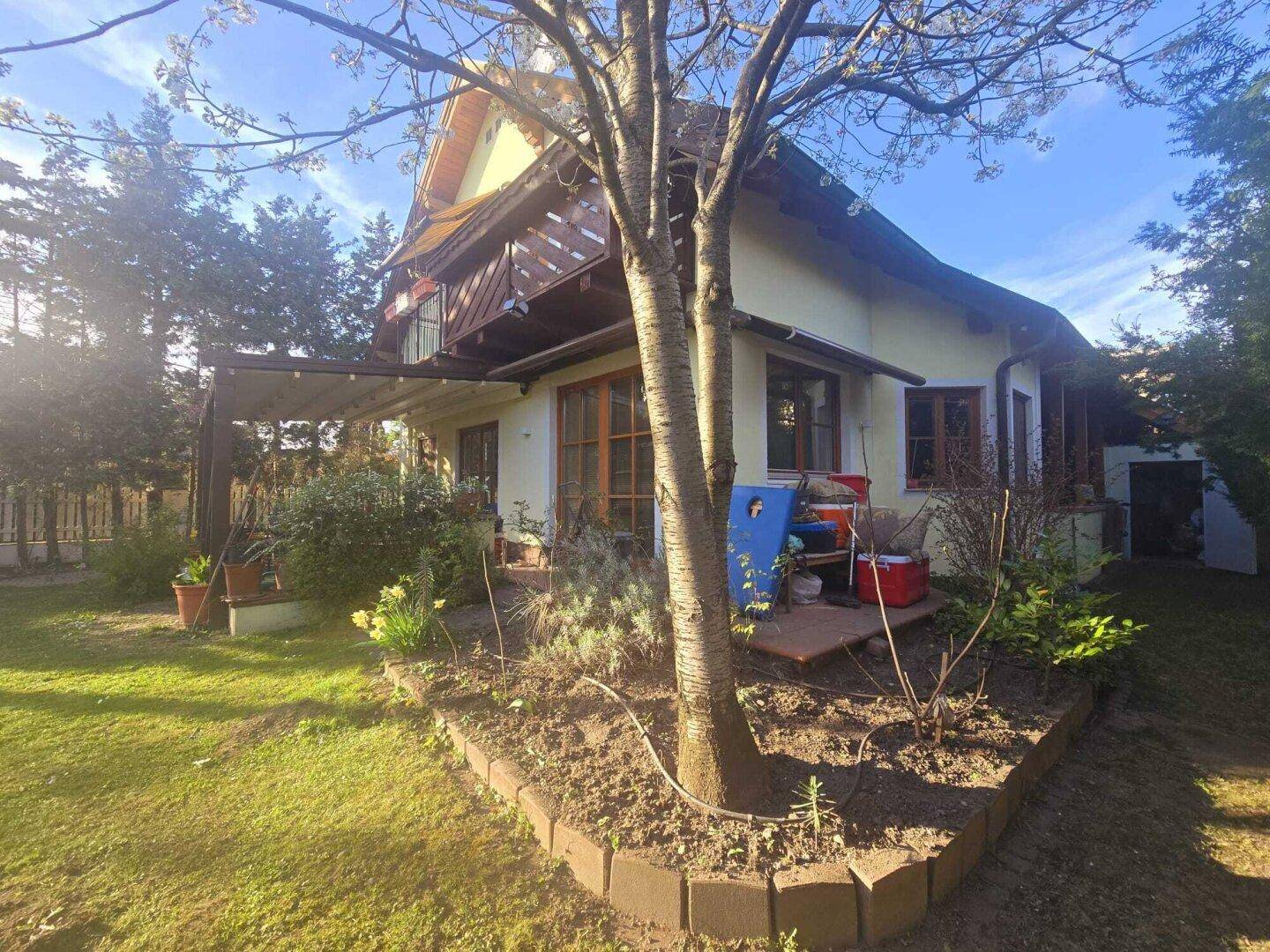 Gartenansicht des Hauses mit Rasenfläche, Blumenbeeten und einer überdachten Terrasse.