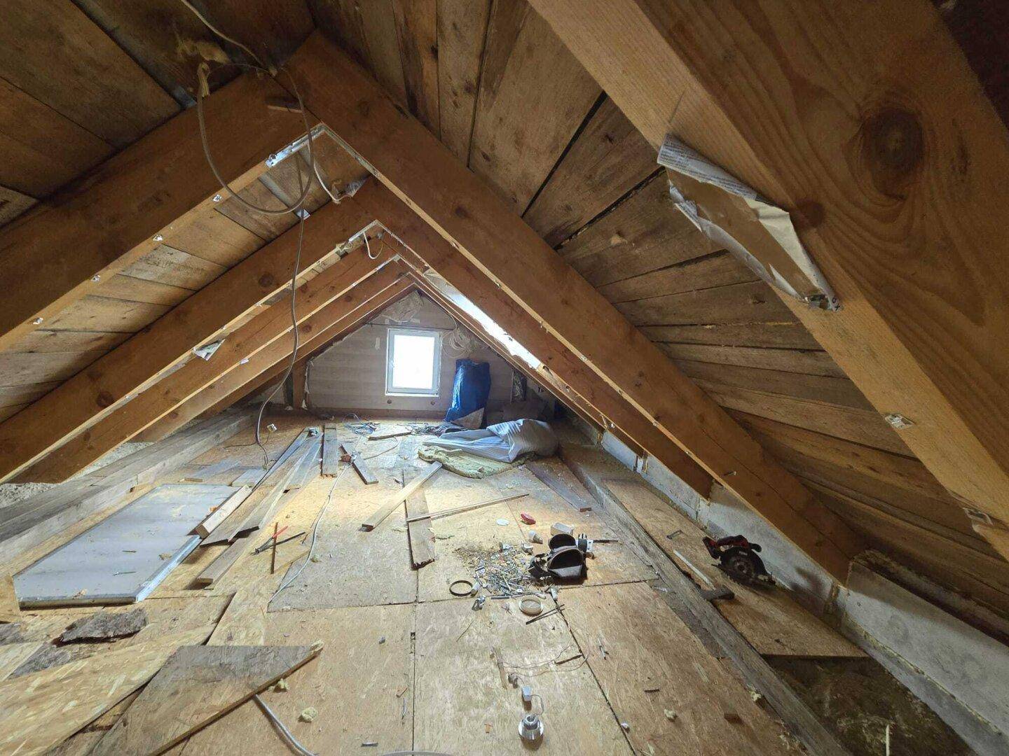 Unausgebauter Dachboden mit sichtbaren Holzbalken und einem kleinen Dachfenster.