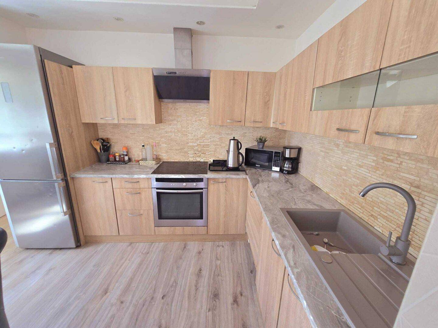 Moderne Einbauküche mit hellen Holzfronten, grauer Arbeitsplatte und integrierten Geräten.