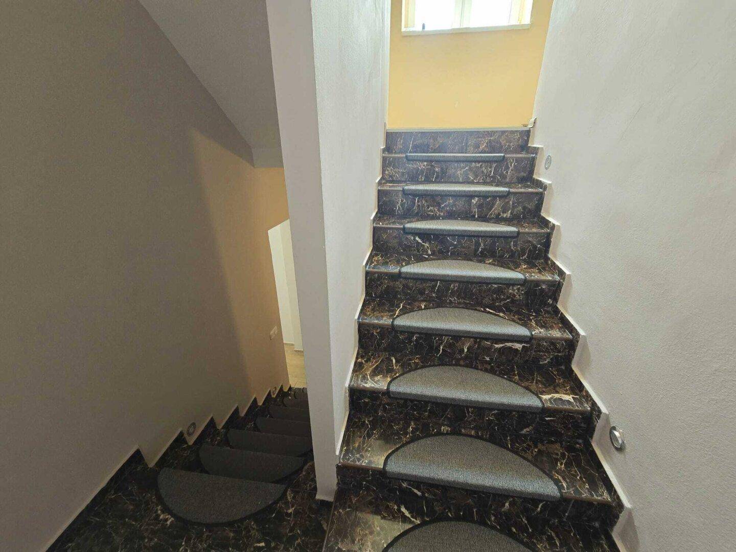 Treppenhaus mit dunklem Marmorboden und Teppichstufen, das in die oberen Stockwerke führt.