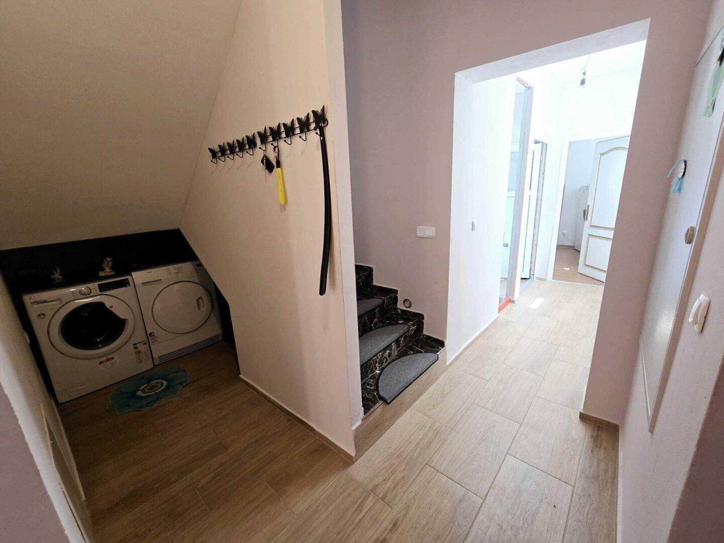 Flur mit Laminatboden, Treppenaufgang und einer Nische für Waschmaschine und Trockner.