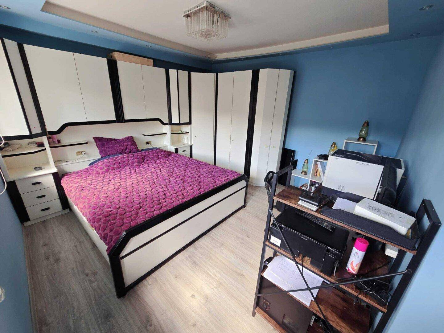 Schlafzimmer mit blau gestrichenen Wänden, großem Bett und weißen Einbauschränken.