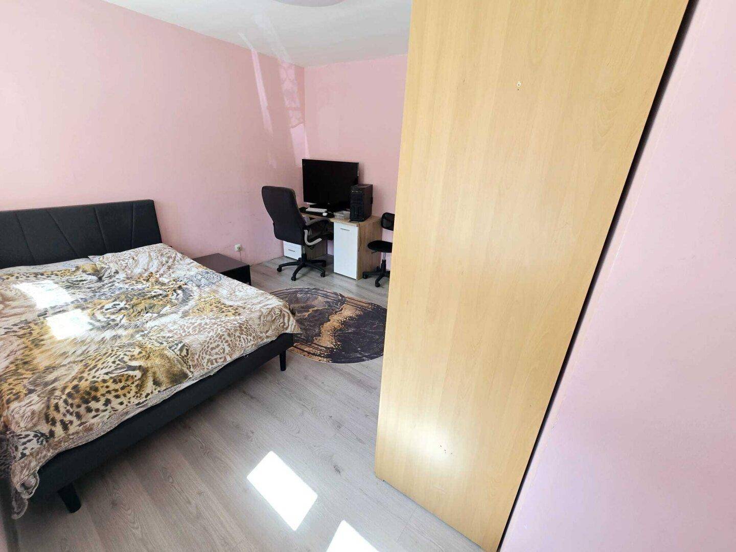 Schlafzimmer mit rosa Wänden, Doppelbett und Laminatboden, hell durch ein Fenster.