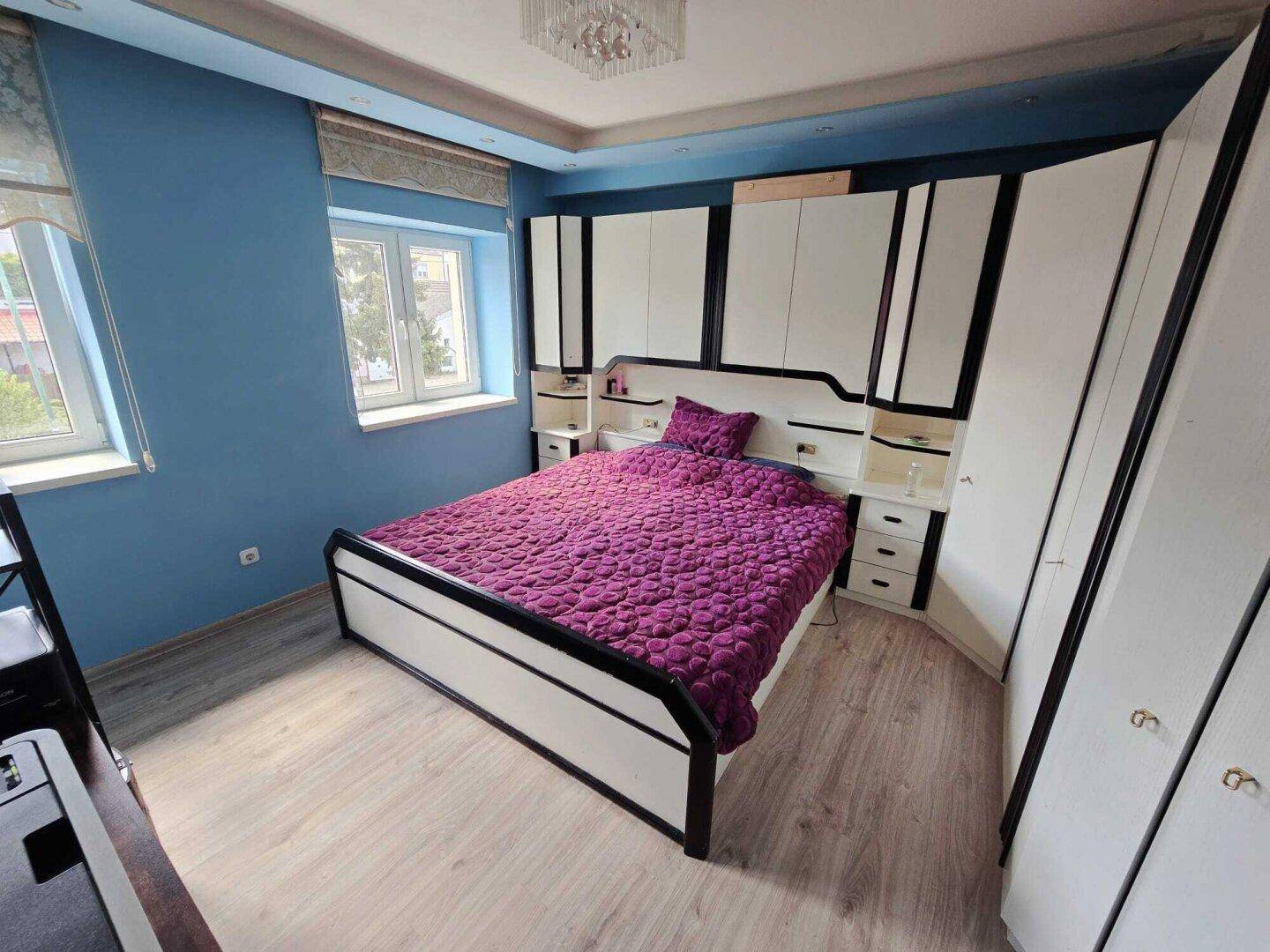 Helles Schlafzimmer mit blauen Wänden, großem Bett und integrierten Schränken unter dem Fenster.
