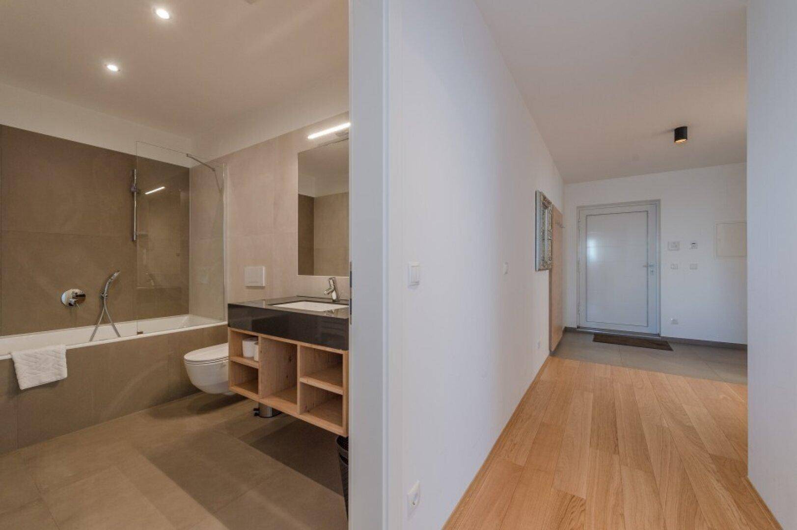 Blick vom Flur in ein modernes Badezimmer mit Badewanne, Dusche und stilvollem Waschtisch.