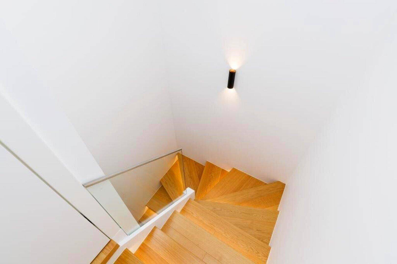 Moderne Holztreppe mit Glasgeländer, die die verschiedenen Ebenen der Wohnung verbindet.