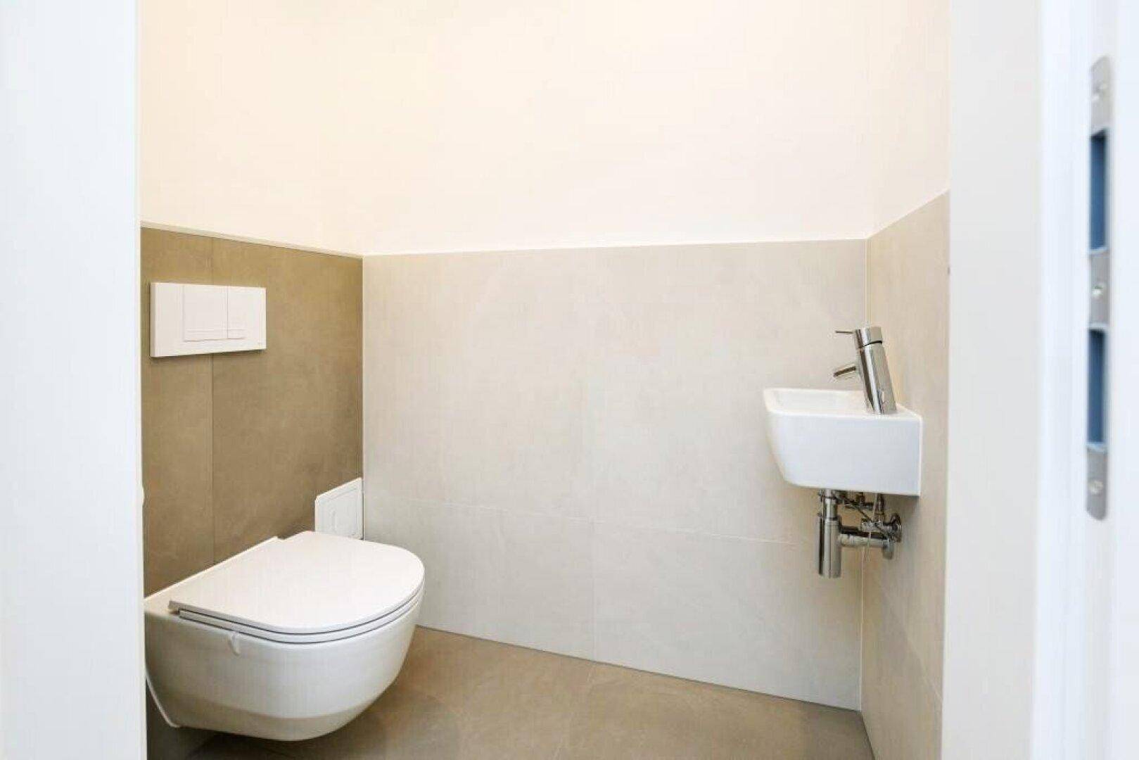 Modernes Gäste-WC mit wandhängender Toilette und kleinem Waschbecken, halbhoch gefliest.