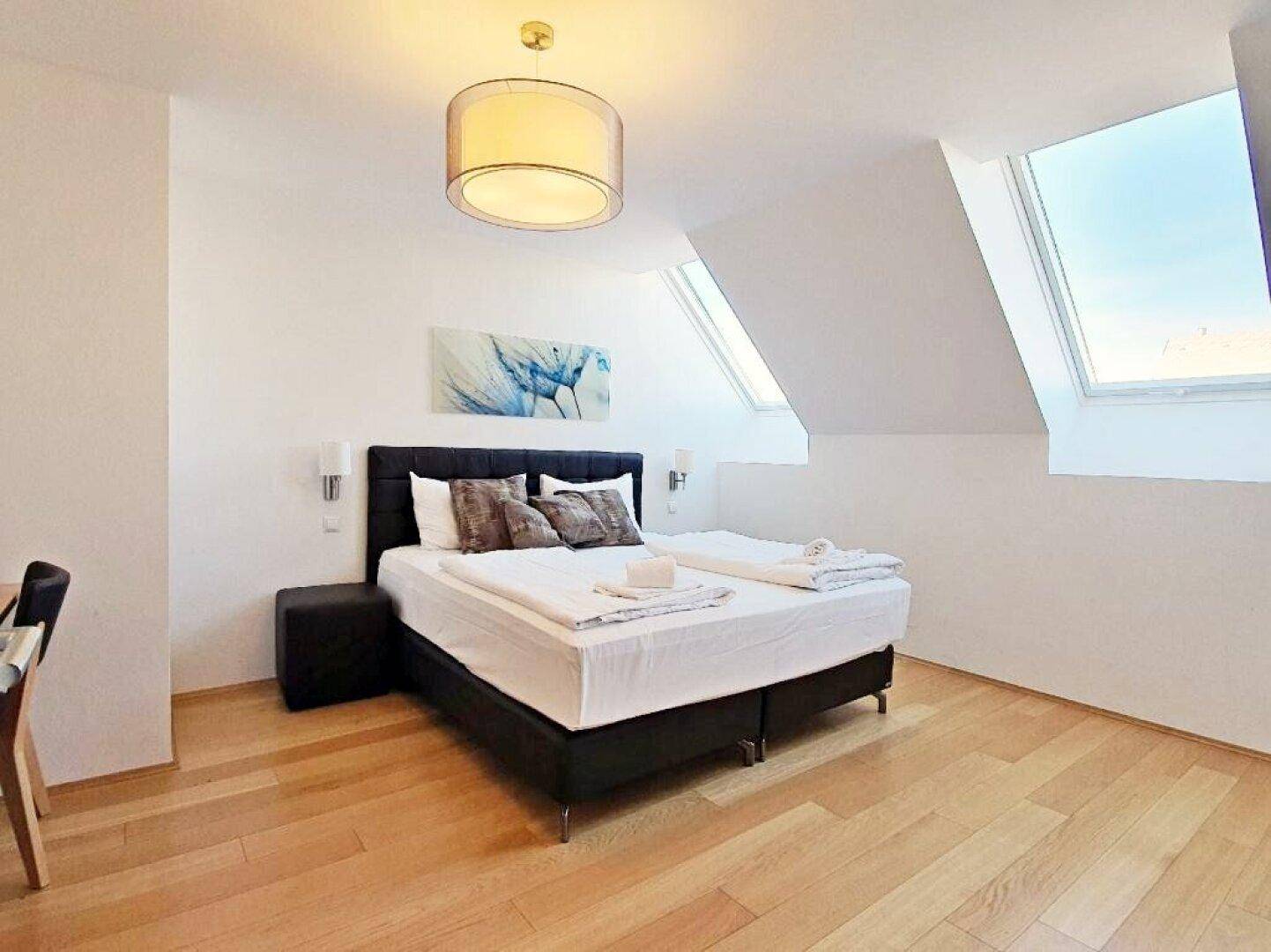 Helles Schlafzimmer mit Doppelbett, Holzboden und Dachschrägen mit integrierten Dachfenstern.