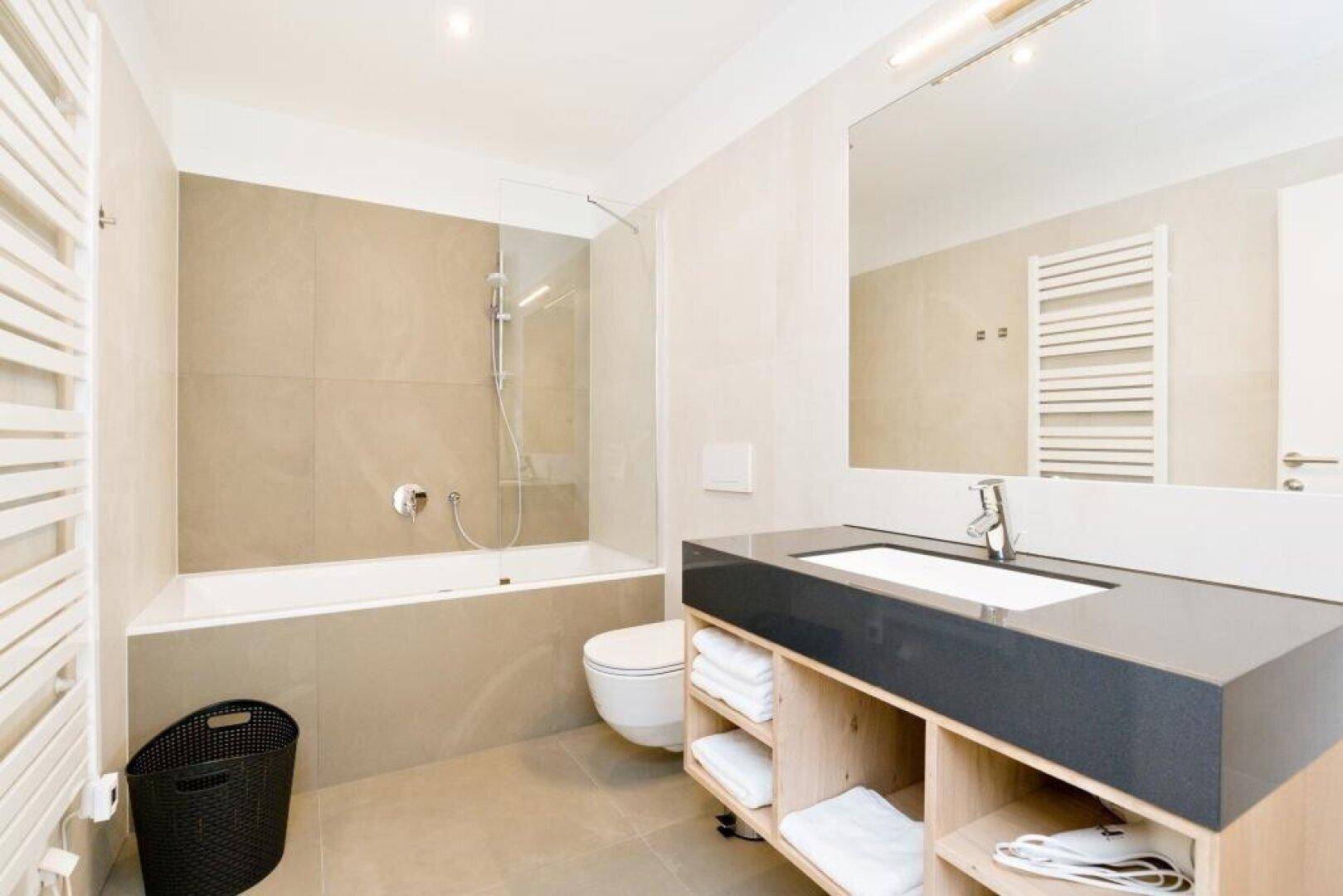 Modernes Badezimmer mit Badewanne, Dusche, wandhängender Toilette und beheiztem Handtuchhalter.