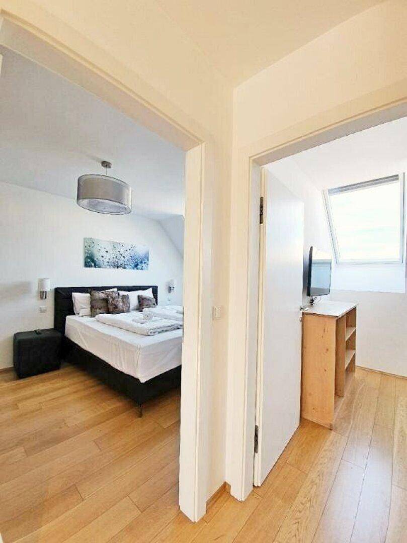 Blick vom Flur in ein helles Schlafzimmer mit Doppelbett und einem großen Dachfenster.