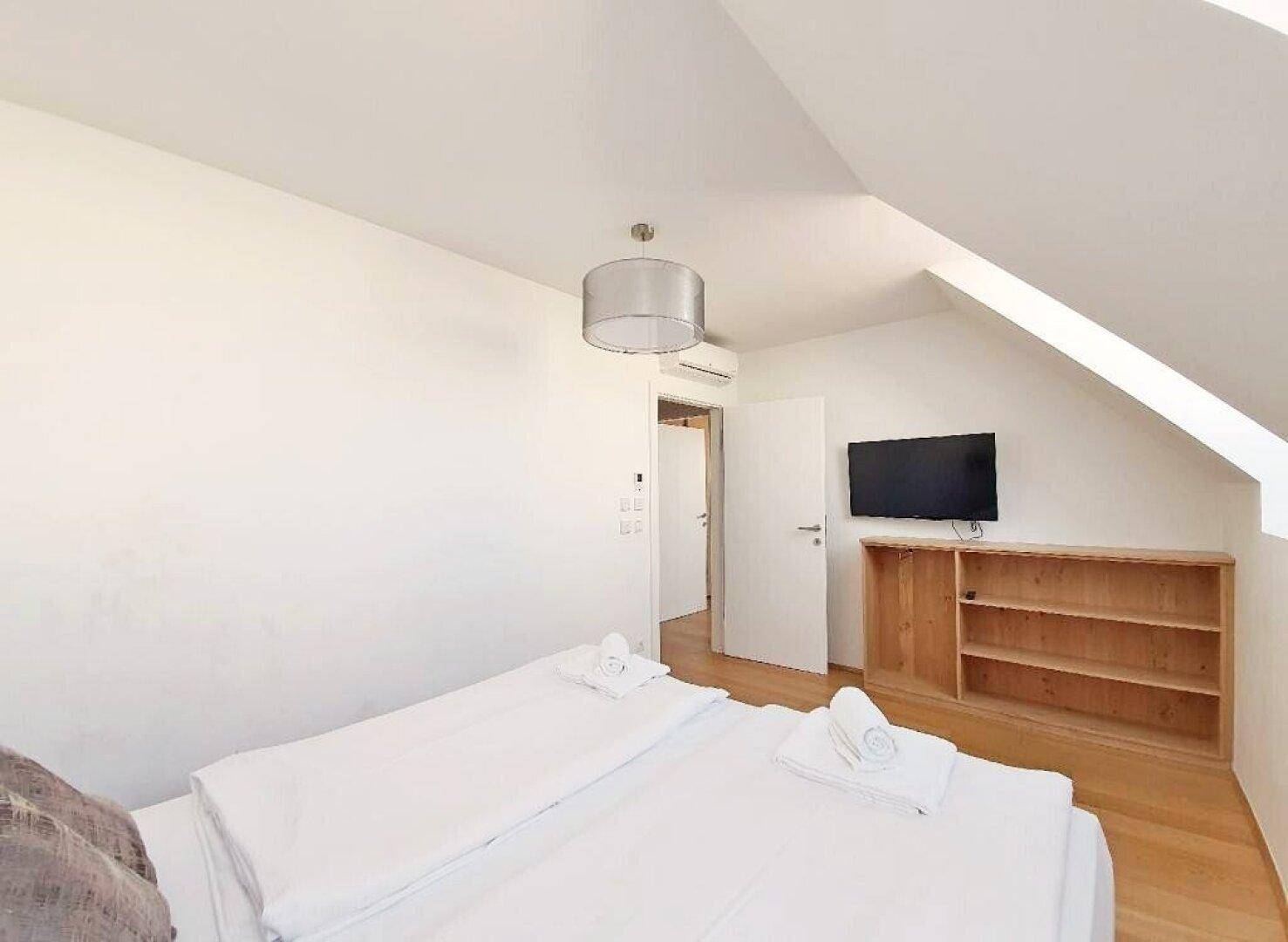 Schlafzimmer mit Doppelbett, Fernseher auf einem Regal und Klimaanlage unter der Dachschräge.