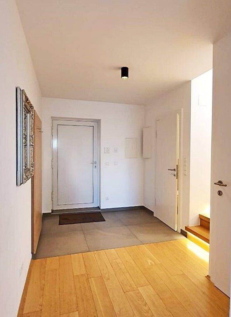 Eingangsbereich mit Fliesenboden, der in Holzboden übergeht, und der Haupttür der Wohnung.