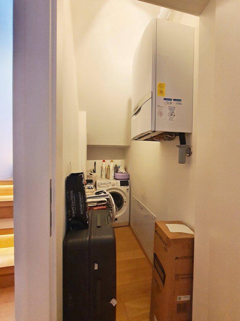 Praktischer Hauswirtschaftsraum mit Waschmaschine und Warmwasserbereiter unter einer Dachschräge.