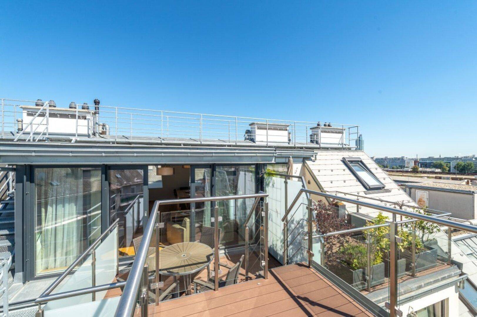 Mehrstufige Dachterrasse mit Sitzgelegenheiten und Glasgeländern, die einen Blick in den Innenbereich ermöglicht.