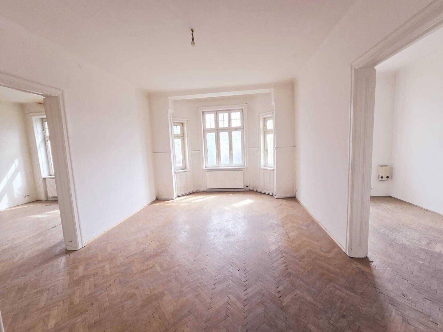 Helles, leeres Zimmer mit Fischgrätparkett, weißen Wänden und einem charmanten Erkerfenster.