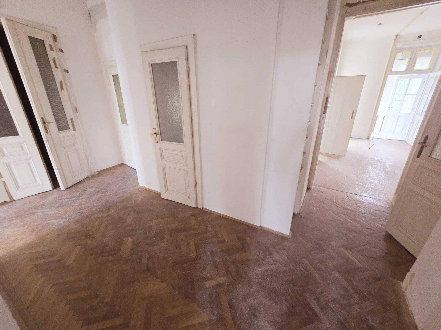 Langer Flur mit Fischgrätparkett und vielen Türen, der die verschiedenen Zimmer verbindet.