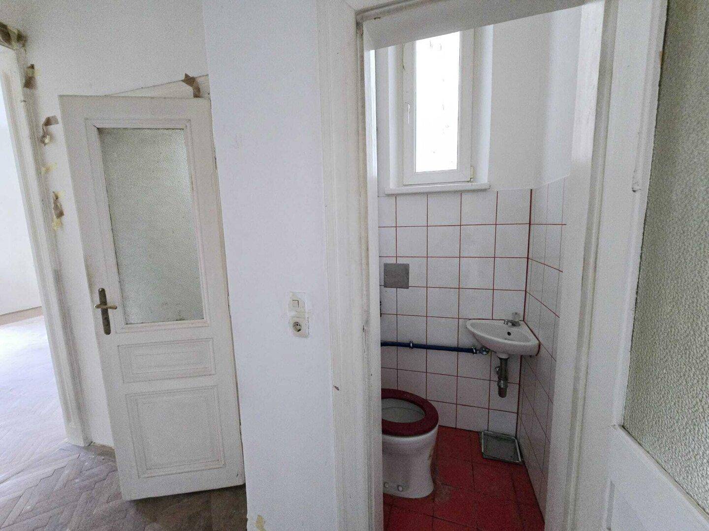 Kleines Gäste-WC mit roten Fliesen, weiß gefliesten Wänden und einem Fenster.