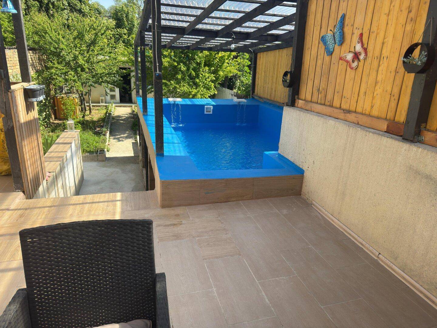 Geräumige Terrasse mit einem erhöhten Pool und Sitzgelegenheiten im Freien, umgeben von viel Grün.