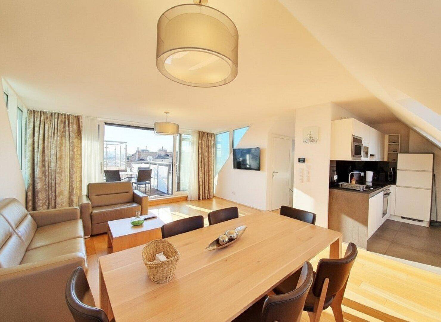 Offener Wohn-Essbereich mit integrierter moderner Küche, Holzboden und Zugang zur Terrasse.
