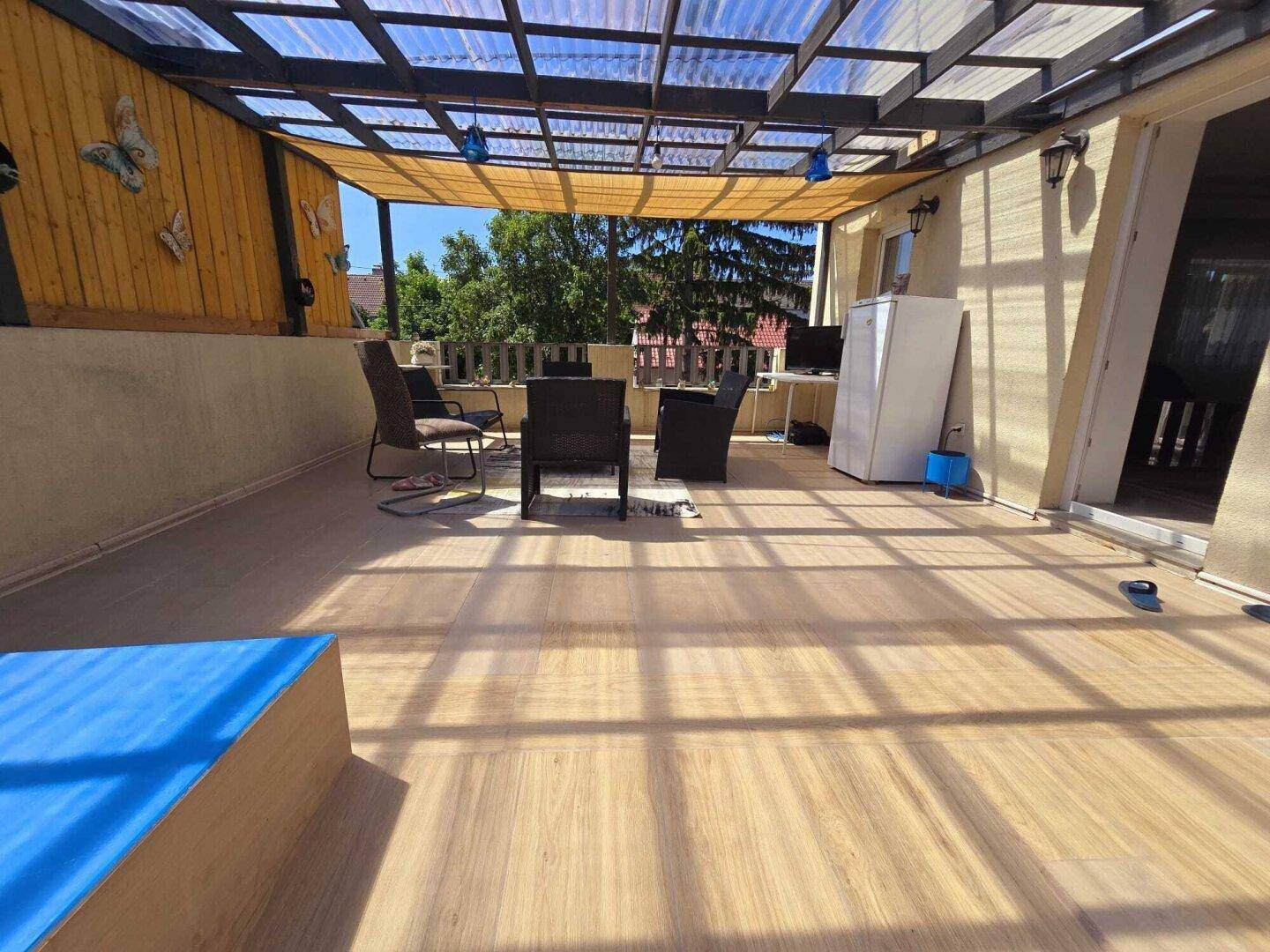 Geräumige überdachte Terrasse mit Holzbodenoptik und Sitzgelegenheiten im Freien.