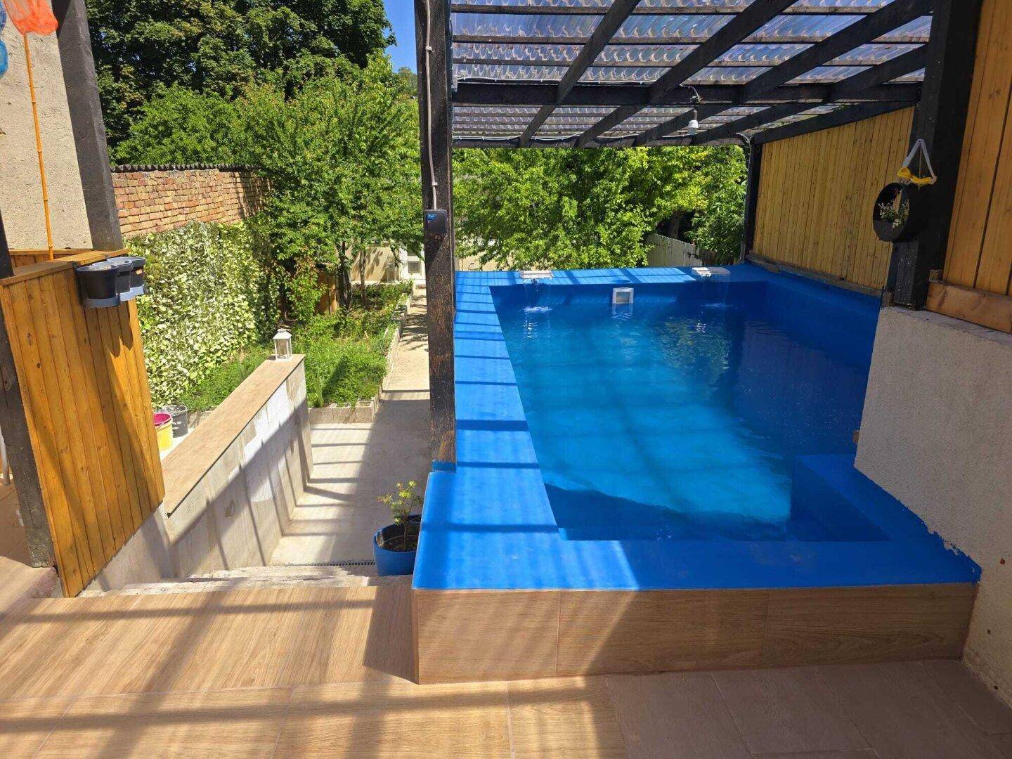 Blauer Swimmingpool auf einer Terrasse mit Treppenzugang zum unteren Gartenbereich.