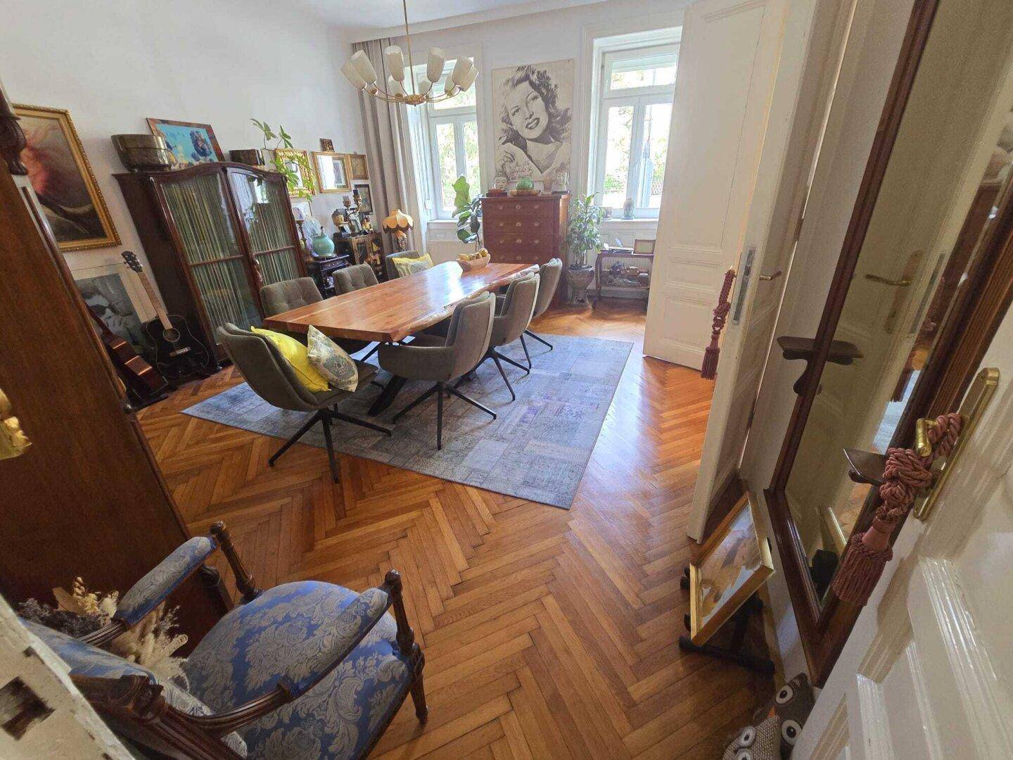 Helles Esszimmer mit Holztisch, Fischgrätparkett und Fenstern, die viel Tageslicht hereinlassen.