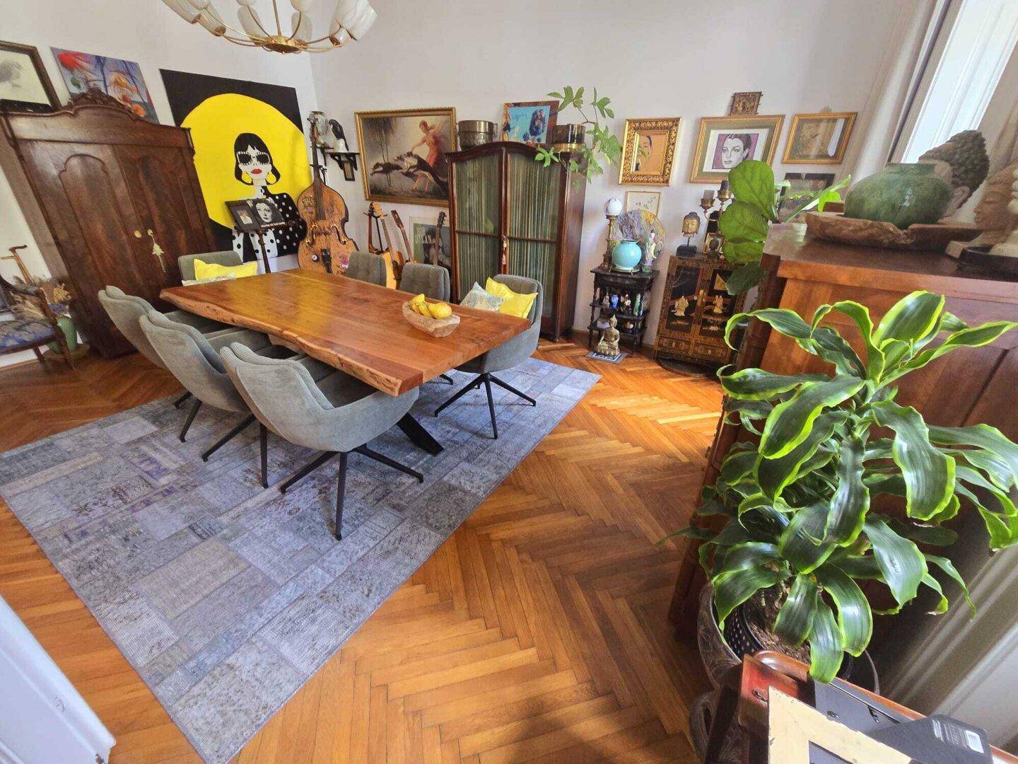 Stilvolles Esszimmer mit großem Holztisch, Fischgrätparkett und vielfältiger Kunstdekoration.