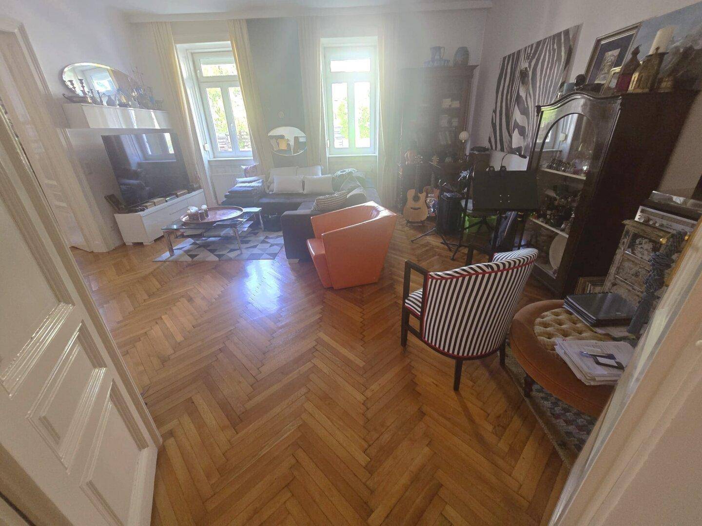Geräumiges Wohnzimmer mit großem Sofa, Fischgrätparkett und hellen Fenstern für viel Tageslicht.