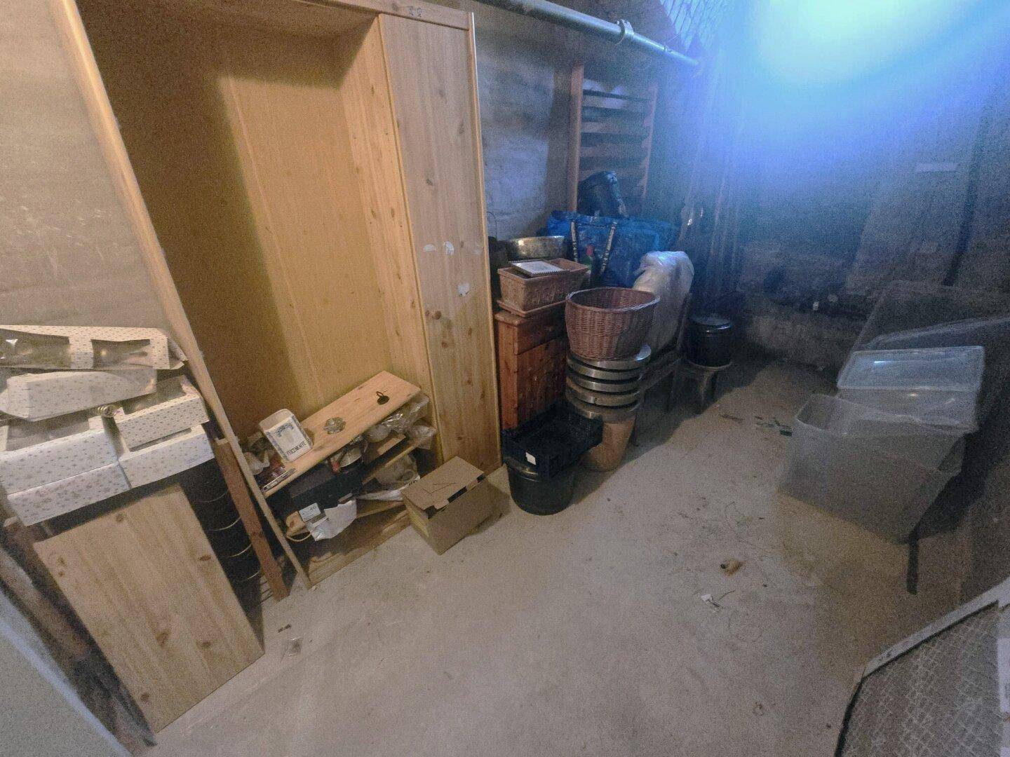 Dunkler Abstellraum im Keller mit verschiedenen Lagergegenständen und Holzregalen.