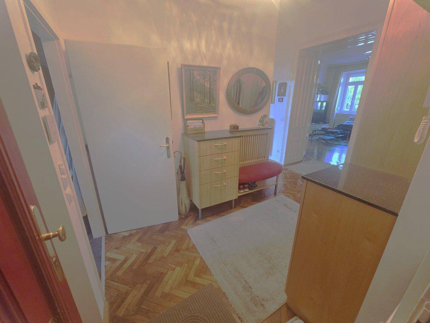 Heller Flur mit Fischgrätparkett, Garderobe und Spiegel, der zu den Wohnbereichen führt.