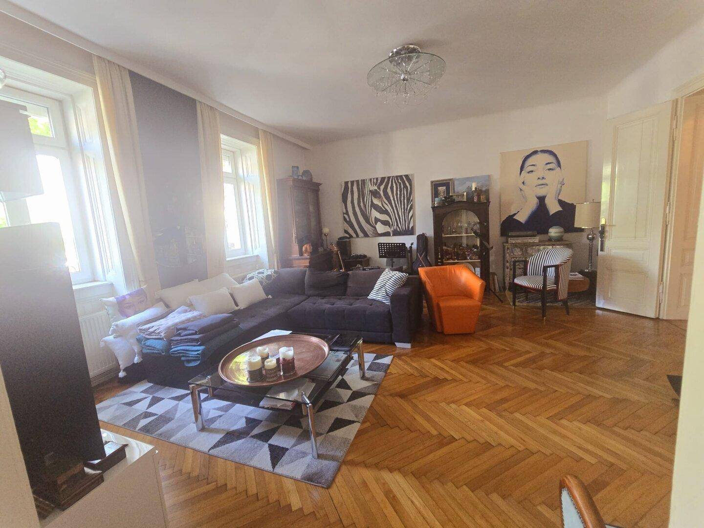 Gemütliches Wohnzimmer mit großem Ecksofa, Fischgrätparkett und viel Tageslicht durch die Fenster.
