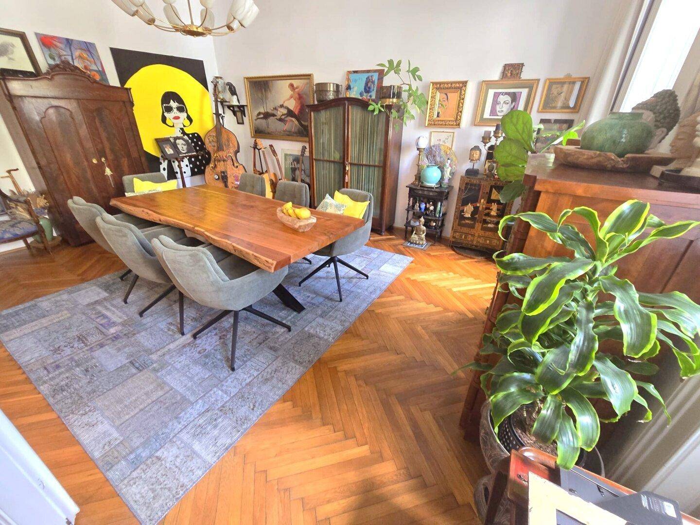Stilvolles Esszimmer mit großem Holztisch, Fischgrätparkett und vielfältiger Kunstdekoration.