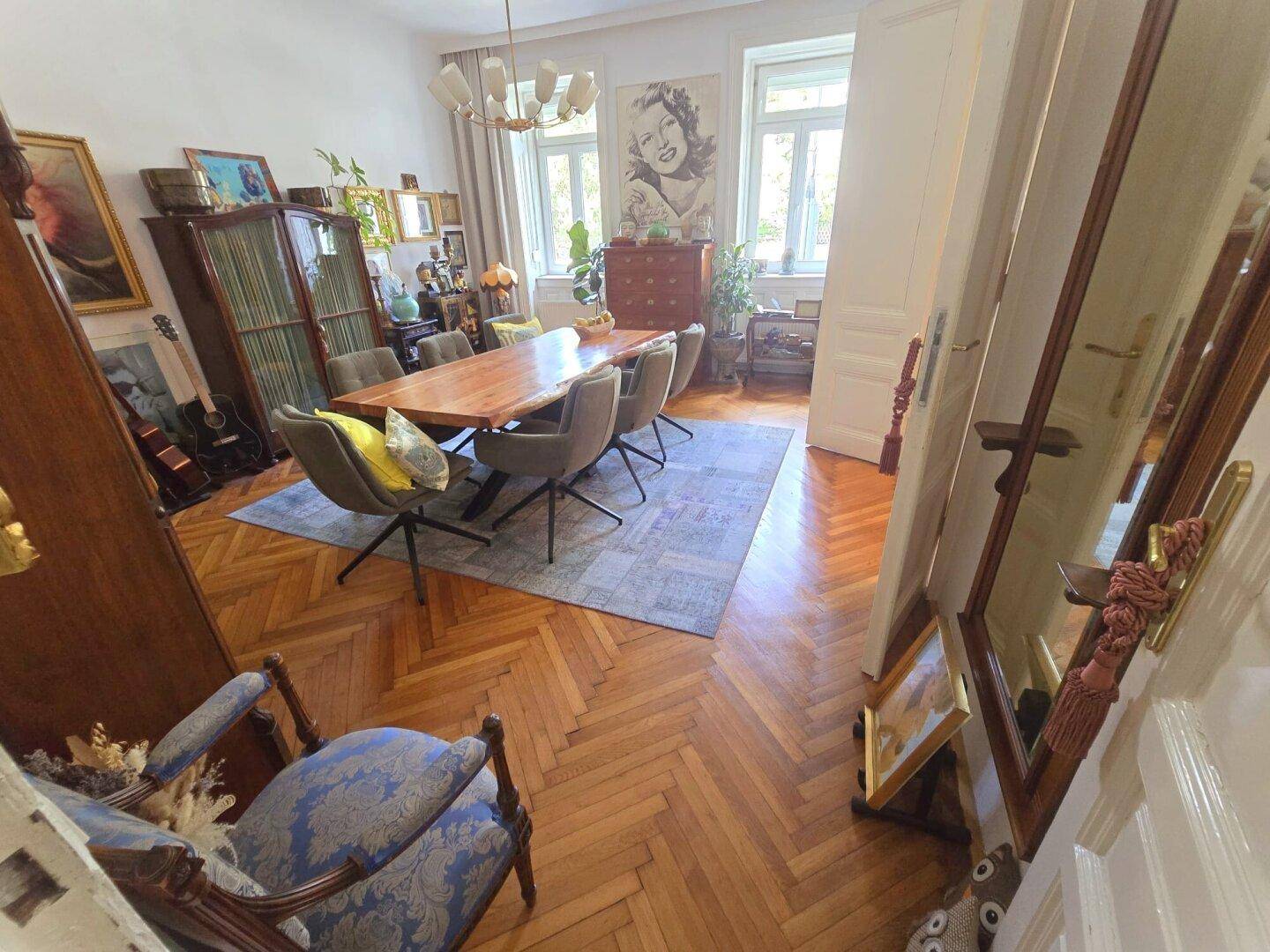 Helles Esszimmer mit Holztisch, Fischgrätparkett und Fenstern, die viel Tageslicht hereinlassen.