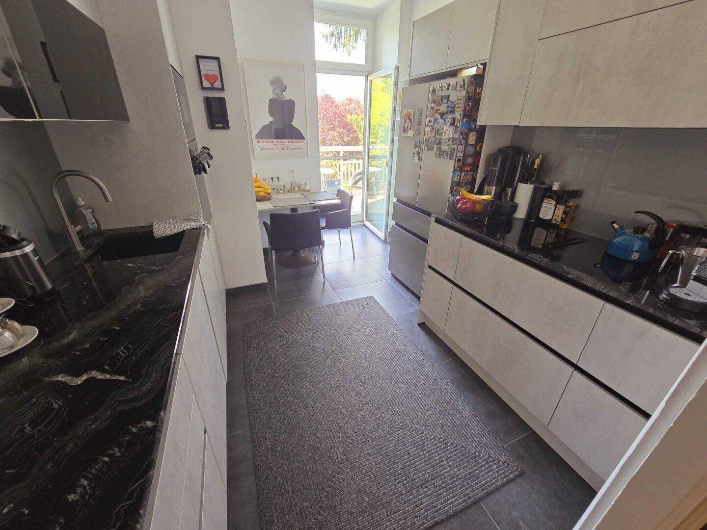 Moderne Küche mit schwarzen Arbeitsplatten, Fliesenboden und Zugang zu einem sonnigen Außenbereich.