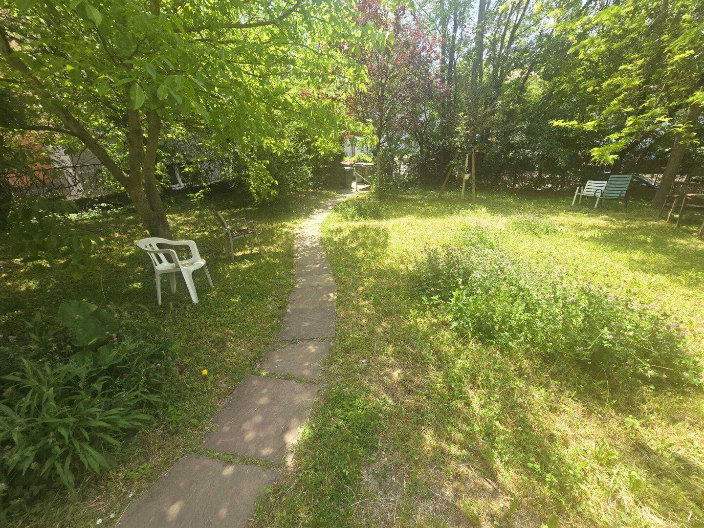 Gepflegter Garten mit einem Steinweg, Rasen und schattenspendenden Bäumen.
