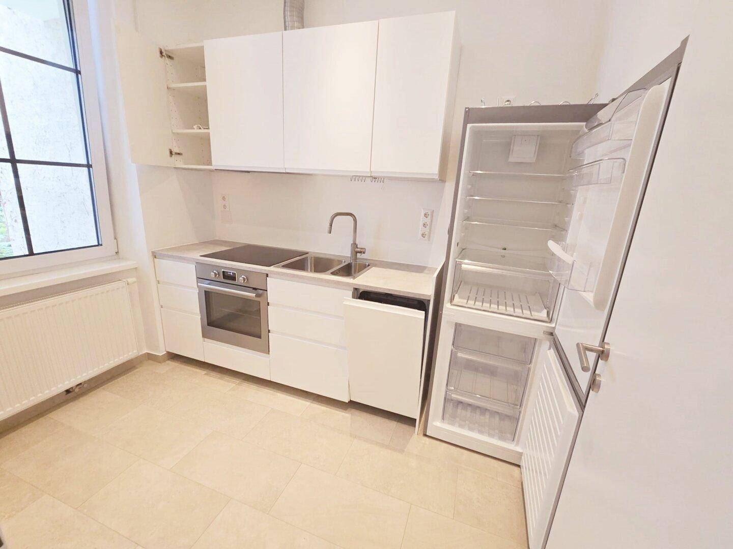 Moderne Einbauküche mit weißen Schränken, Induktionskochfeld, Backofen und Kühlschrank.