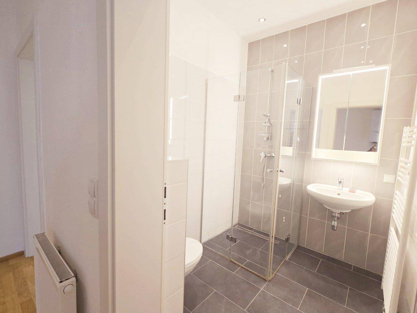 Helles Badezimmer mit moderner Dusche, WC, Einzelwaschbecken und Spiegelschrank.