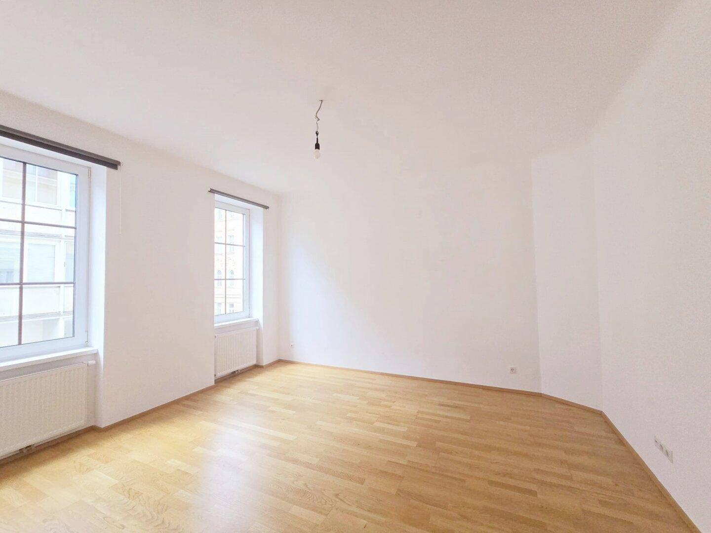 Geräumiges, helles Zimmer mit Holzparkett und großen Fenstern, bereit zur individuellen Gestaltung.