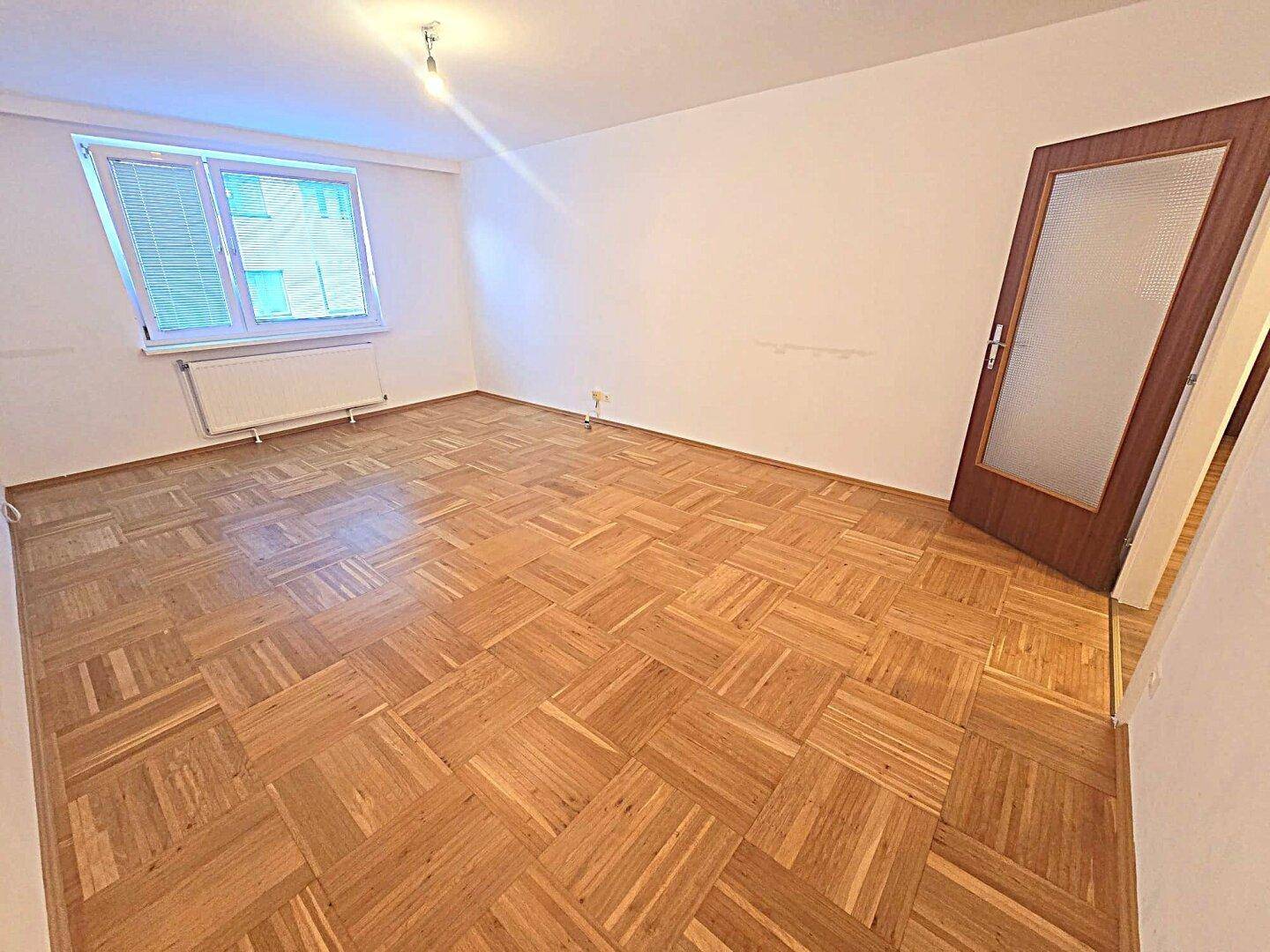 Geräumiges Zimmer mit klassischem Parkettboden und einem Fenster, das viel Tageslicht hereinlässt.