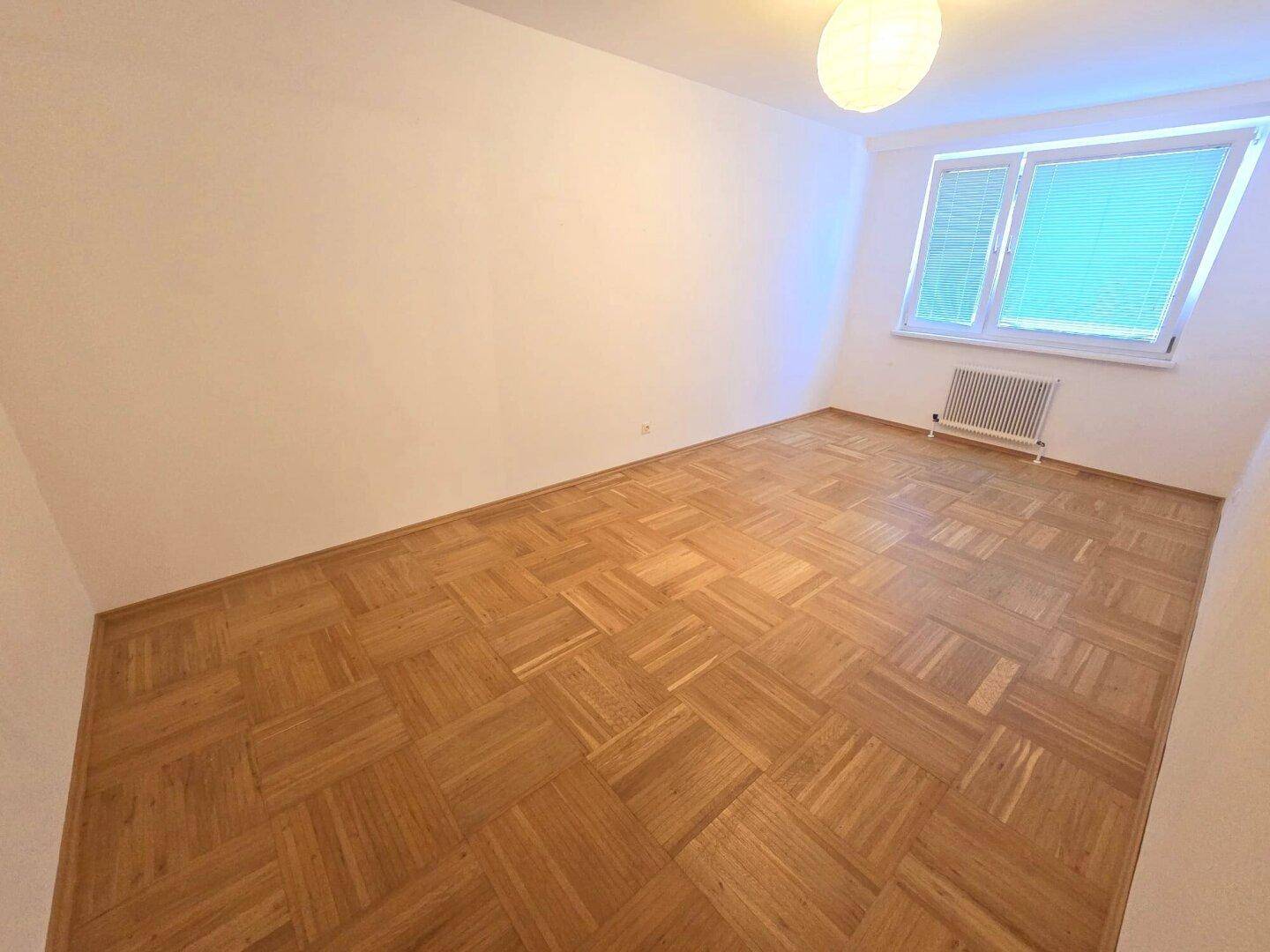 Helles Schlafzimmer mit elegantem Parkettboden und einem Fenster für natürliche Belichtung.